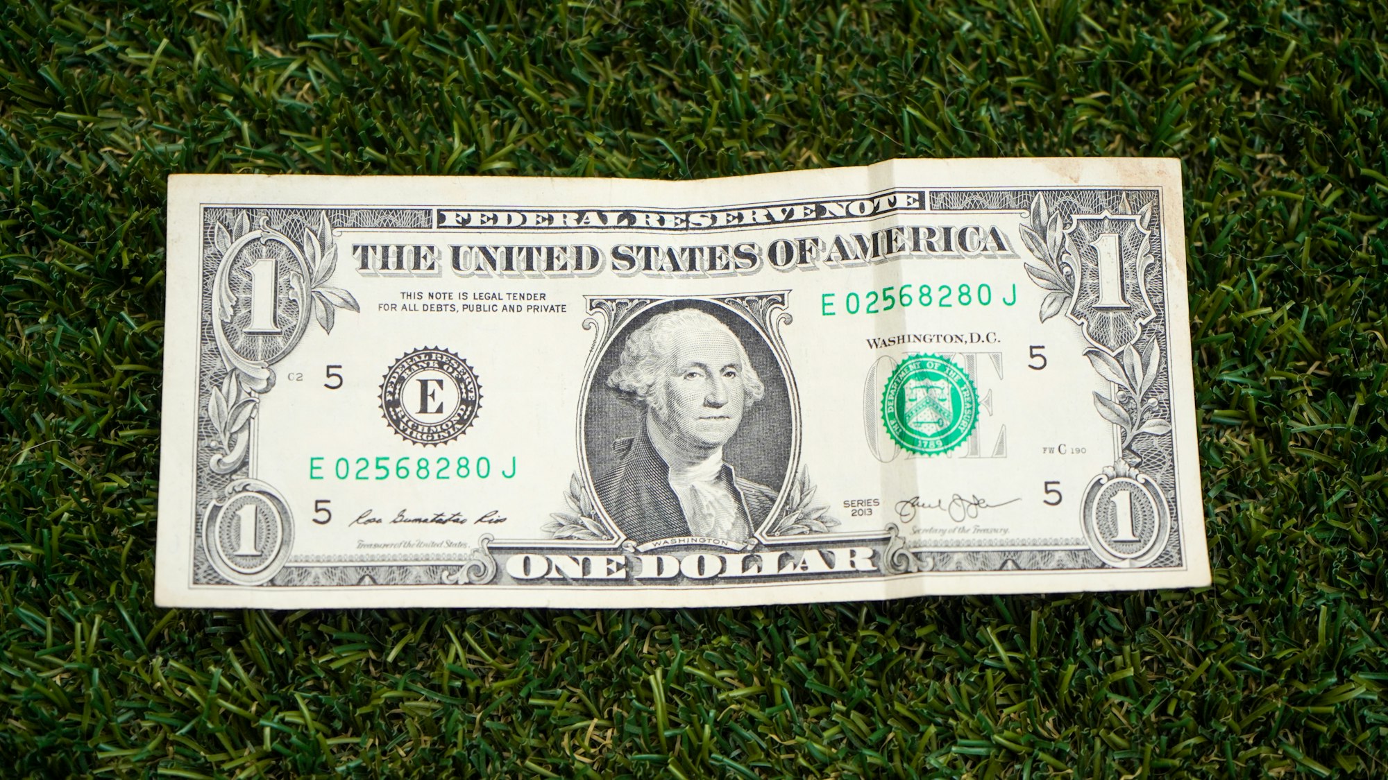 One American dollar bill on the fake grass field.