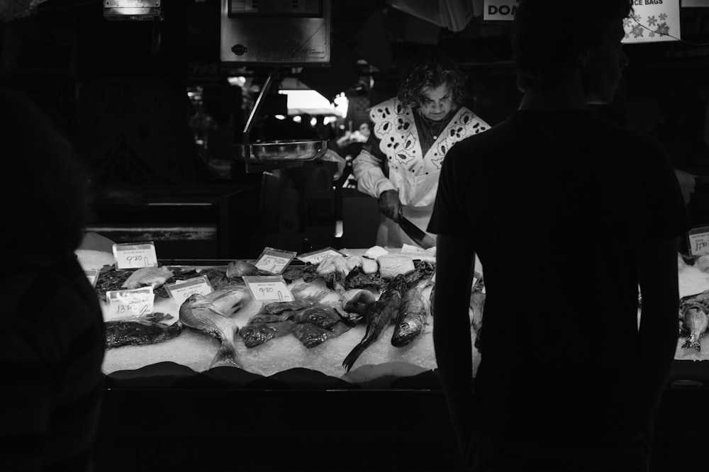 grayscale photo of man and woman standing in front of food