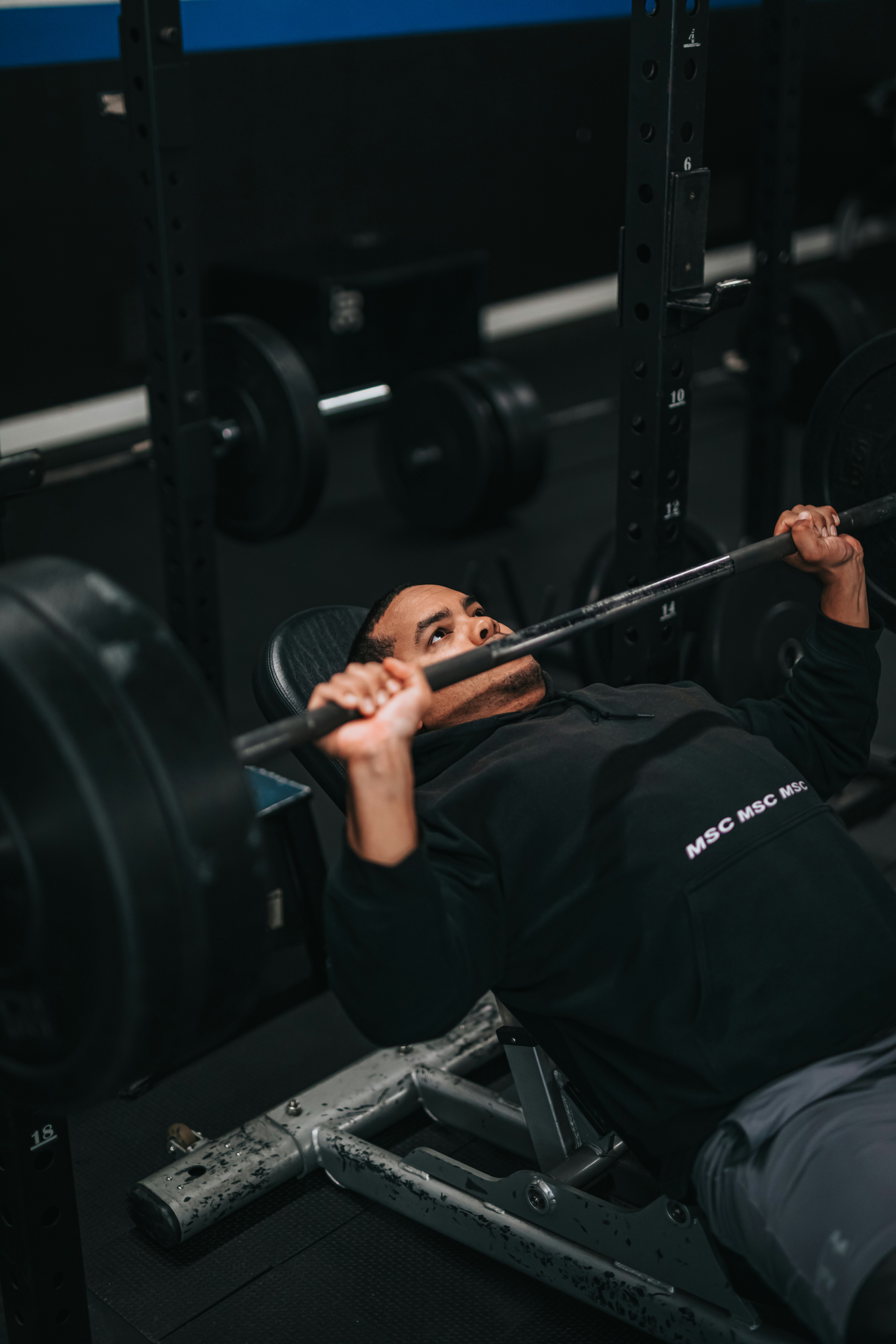 Young man in gym hoodie sitting on bench after workout, low light, natural skin texture, post-workout fatigue