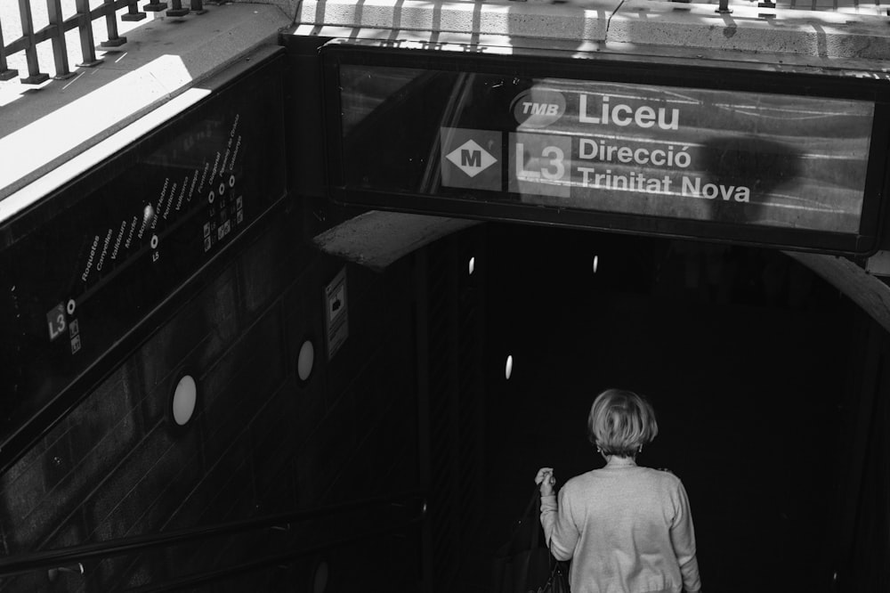 grayscale photo of man in jacket standing in front of the building