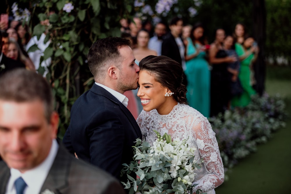 man in black suit kissing woman in white floral dress