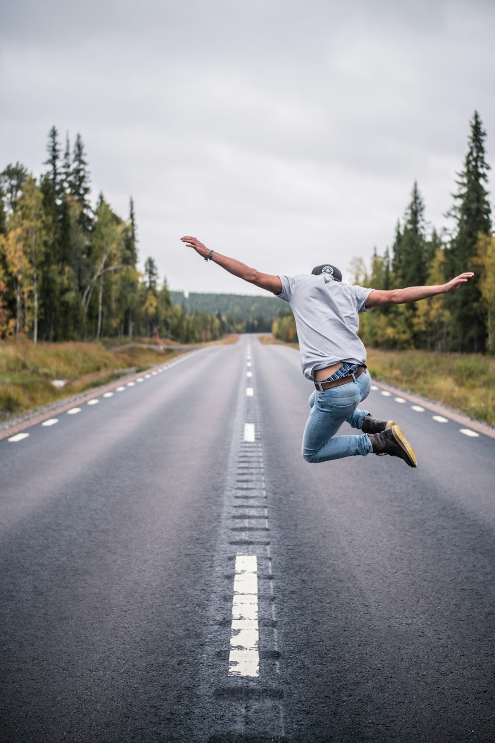 man in white t-shirt and blue denim jeans jumping on the road during daytime