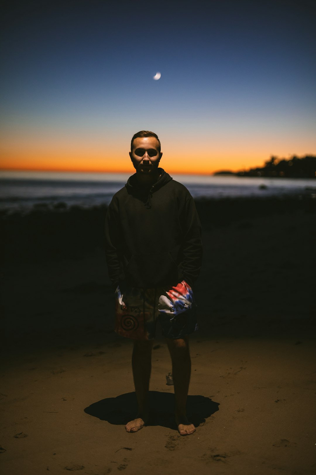 man in black jacket and blue denim shorts standing on beach during sunset