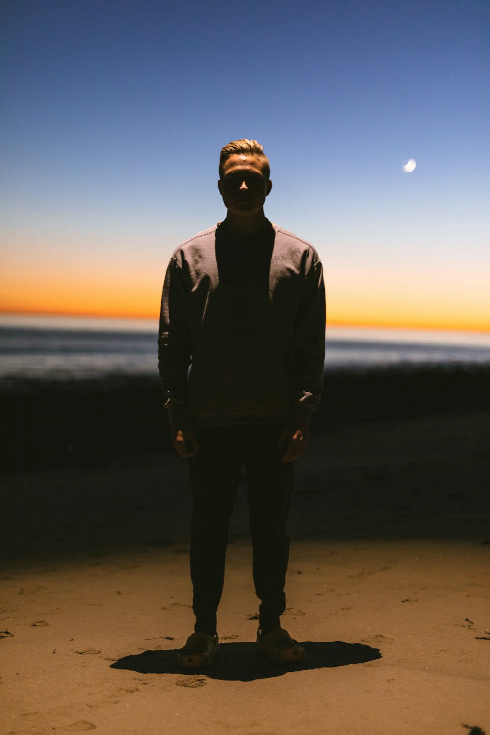 man in black jacket standing on beach during sunset