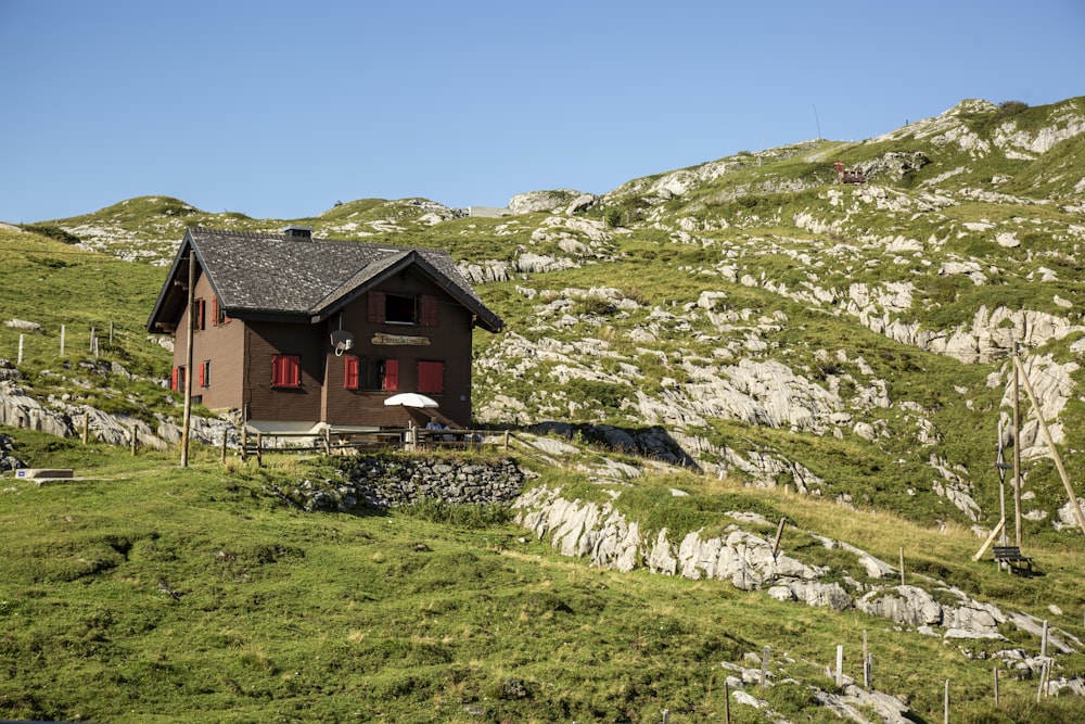 brown and white house on green grass field near mountain under blue sky during daytime