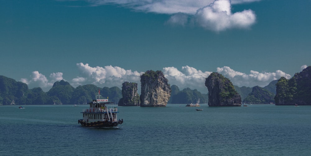 boat on sea near rock formation under blue sky and white clouds during daytime