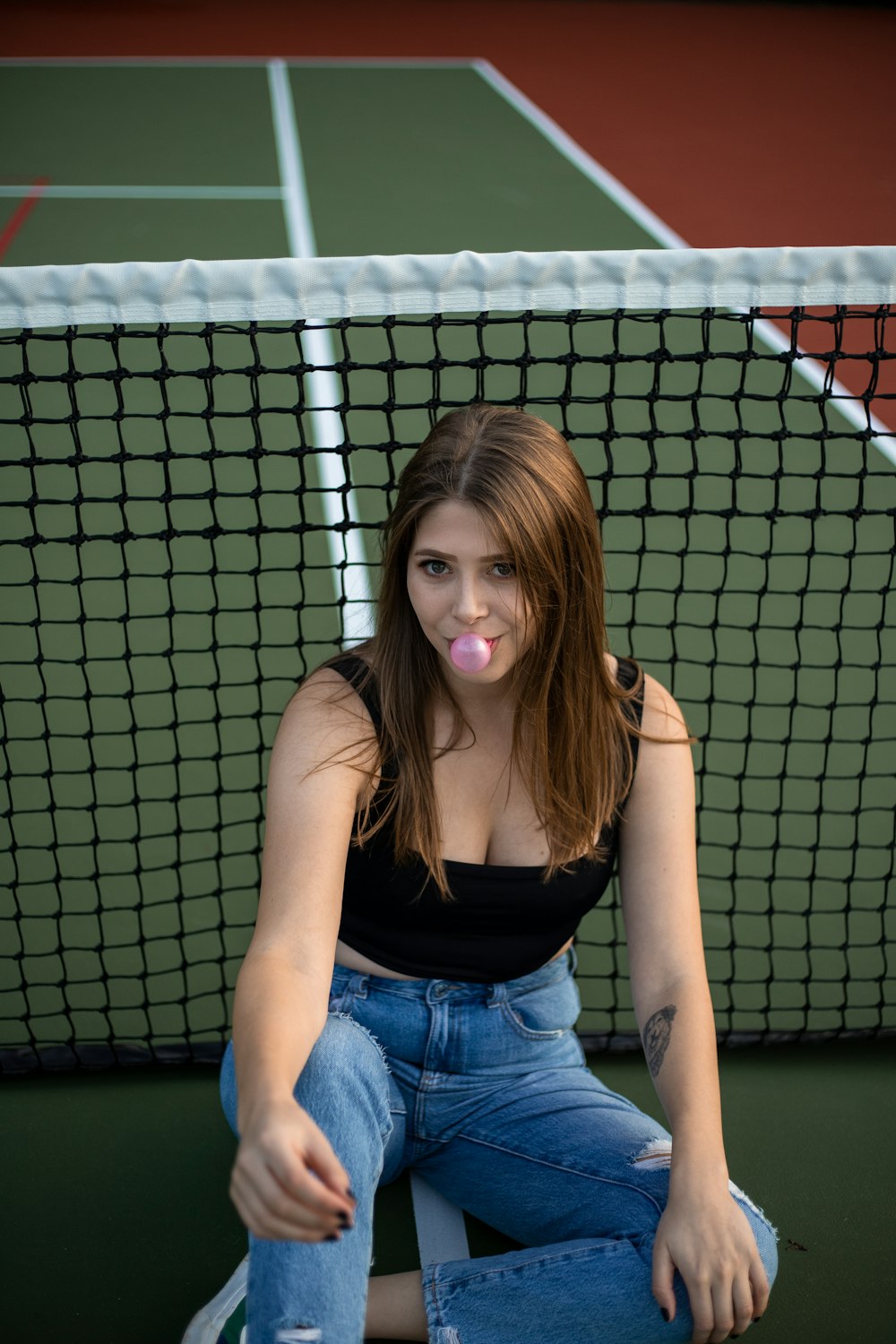 woman in black tank top and blue denim shorts sitting on green metal fence