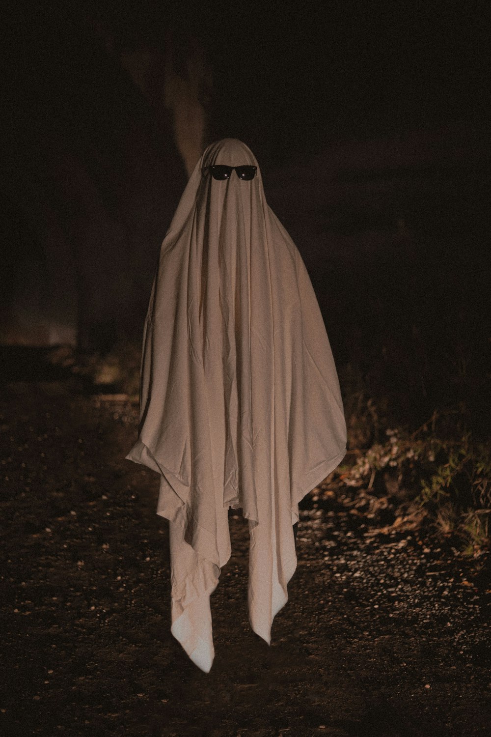 person in white robe standing on brown dried leaves during nighttime