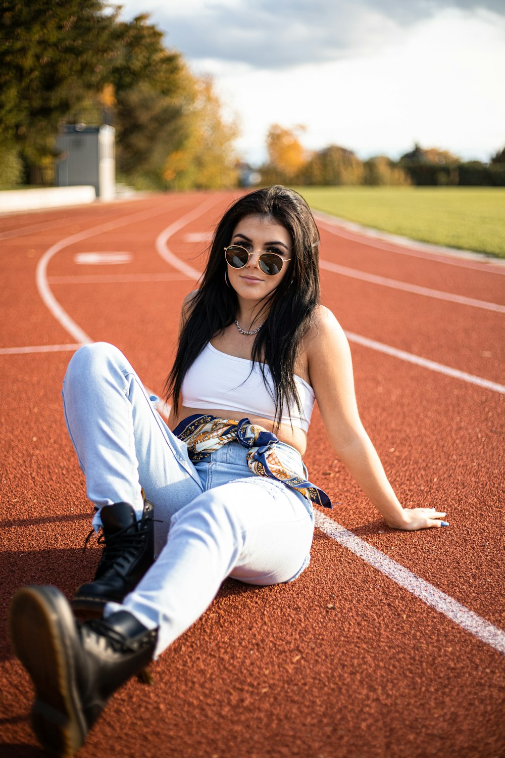woman in white tank top and blue denim jeans sitting on track field during daytime