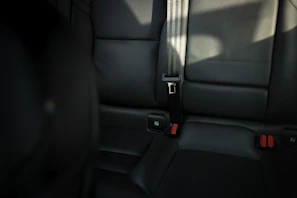 Close-up of a sleek black leather car seat with vibrant red stitching under soft lighting
