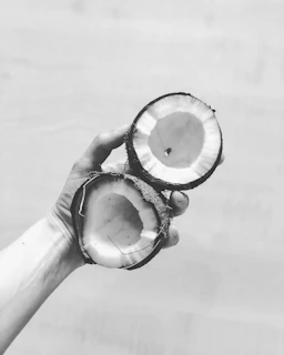 Hands holding a cracked coconut revealing the white flesh inside.