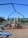 A brightly colored playground set featuring slides, climbing structures, and monkey bars. Red, blue, and green components contrast with the natural surroundings. The playground is situated on a wood chip-covered surface under a clear blue sky with trees in the background.