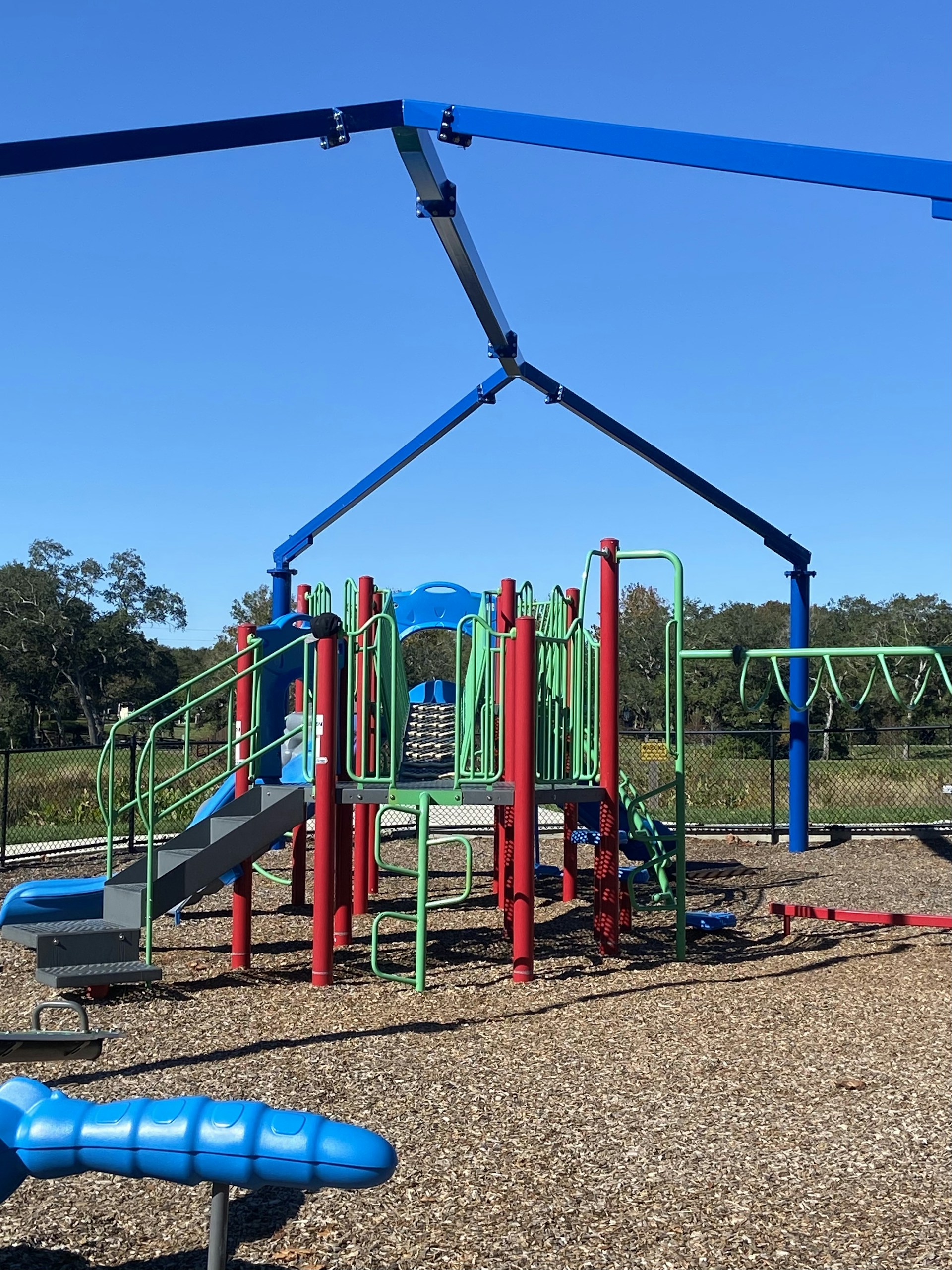 Smiling kids playing together on a safe, pastel-colored playground with soft blue skies overhead.