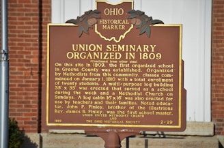 A historical marker sign situated outdoors against a brick background. The sign details the organization of the Union Seminary in 1809, describing its role as the first organized school in Greene County. The marker notes the seminary's educational and religious functions, mentioning a log cabin erected for teachers and families.