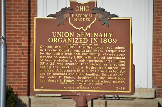 A historical marker sign situated outdoors against a brick background. The sign details the organization of the Union Seminary in 1809, describing its role as the first organized school in Greene County. The marker notes the seminary's educational and religious functions, mentioning a log cabin erected for teachers and families.