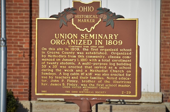A historical marker sign situated outdoors against a brick background. The sign details the organization of the Union Seminary in 1809, describing its role as the first organized school in Greene County. The marker notes the seminary's educational and religious functions, mentioning a log cabin erected for teachers and families.