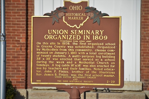 A historical marker sign situated outdoors against a brick background. The sign details the organization of the Union Seminary in 1809, describing its role as the first organized school in Greene County. The marker notes the seminary's educational and religious functions, mentioning a log cabin erected for teachers and families.