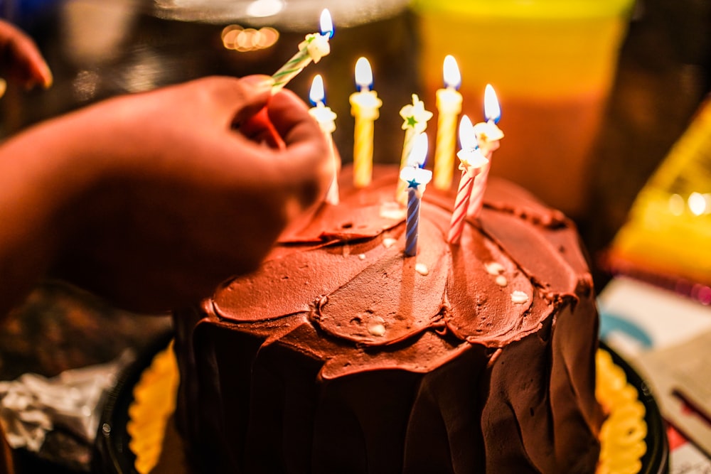person holding lighted candle on brown cake