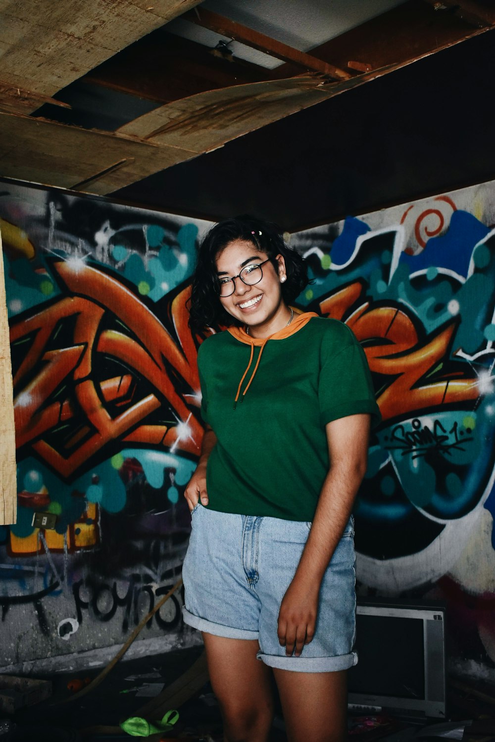 Mujer con camiseta roja de cuello redondo y jeans de mezclilla azul de pie cerca de la pared de graffiti