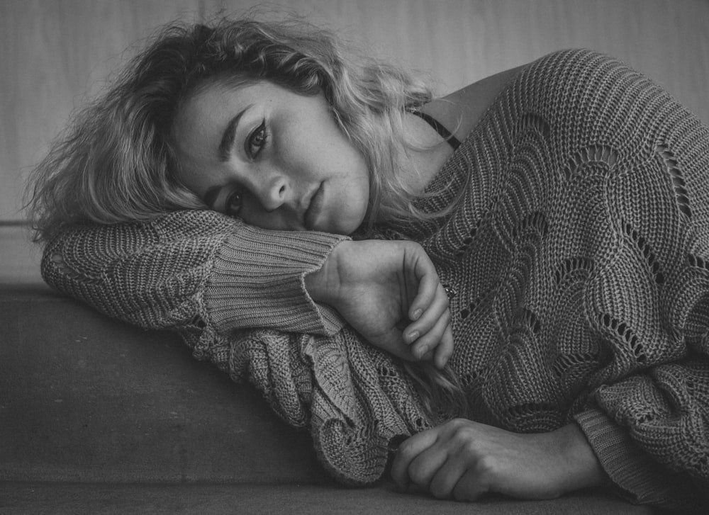 grayscale photo of woman in sweater lying on couch