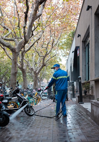 man in blue jacket and blue denim jeans standing beside black motorcycle during daytime