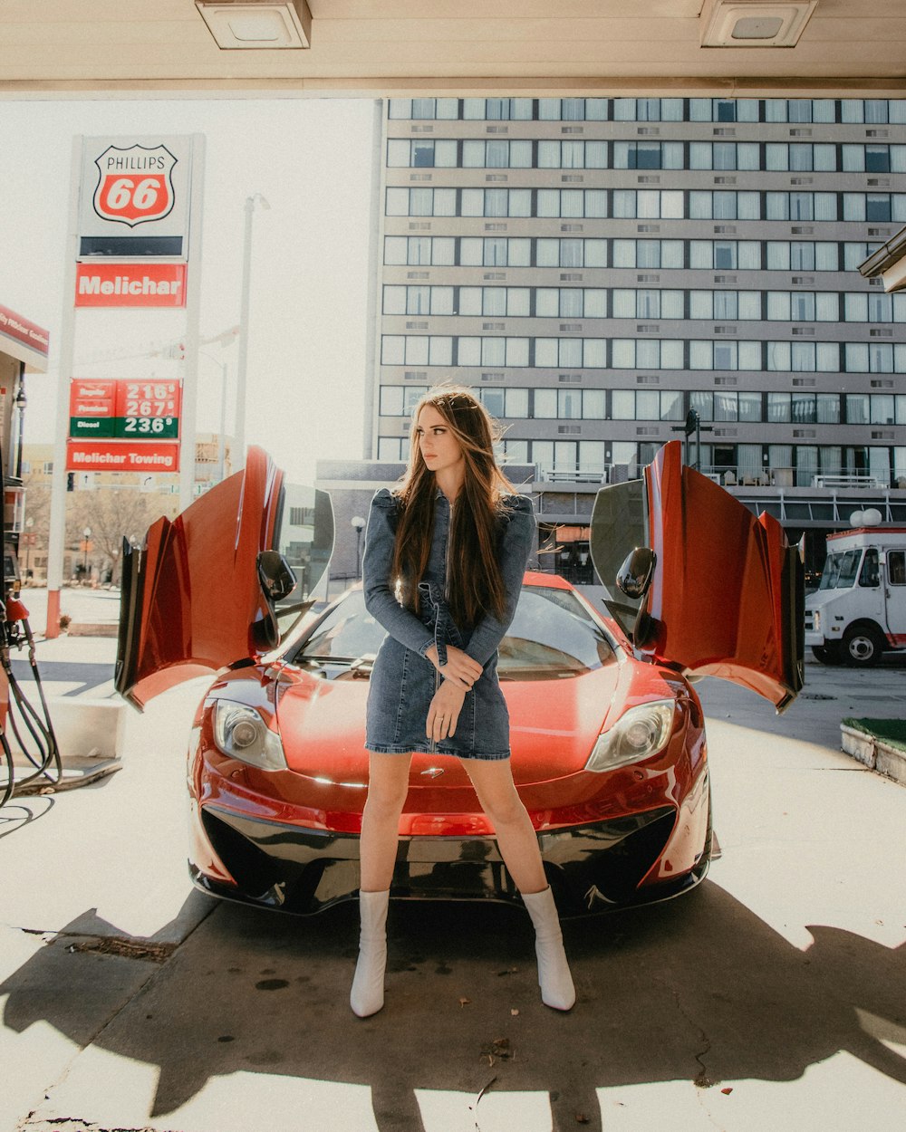 黒い長袖シャツとブルーデニムジーンズの女性が赤いフェラーリ車の横に立つ