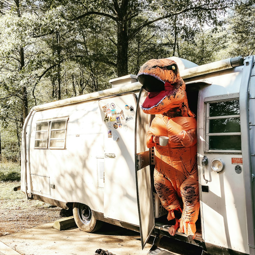 man in orange jacket and brown pants sitting on white van during daytime