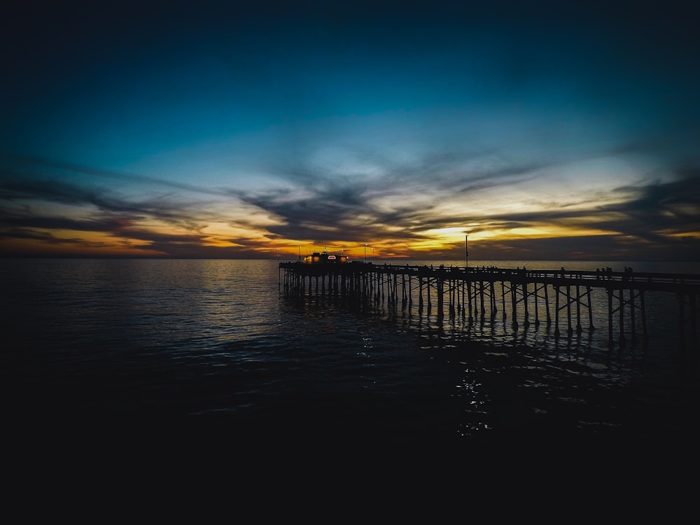 silhouette of dock on body of water during sunset