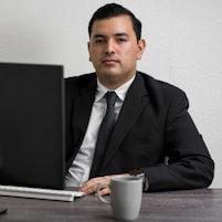 man in black suit jacket holding white ceramic mug