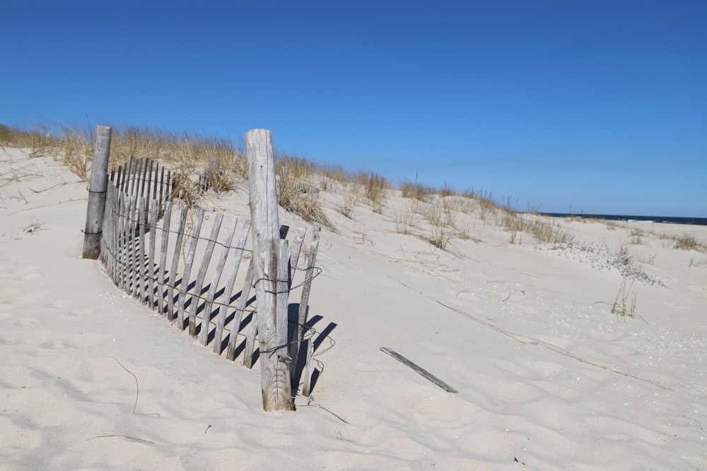 valla de madera marrón en arena blanca bajo cielo azul durante el día