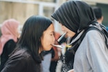 Two people are engaging in a playful activity involving straws and crackers. They are facing each other closely, each holding a cracker with a straw. The focus is on their interaction and concentration. In the background, other people are visible, indicating a social setting.