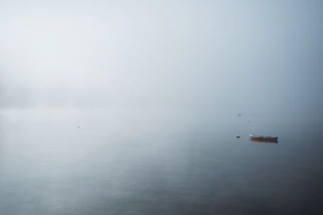 A serene backwater with a small boat, framed by soft morning light and gentle fog.