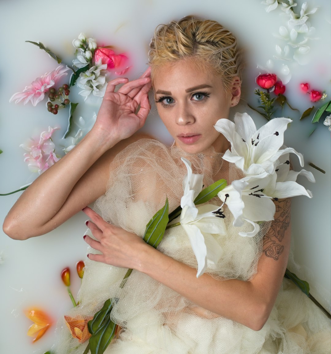 woman in white floral dress lying on white and pink flowers