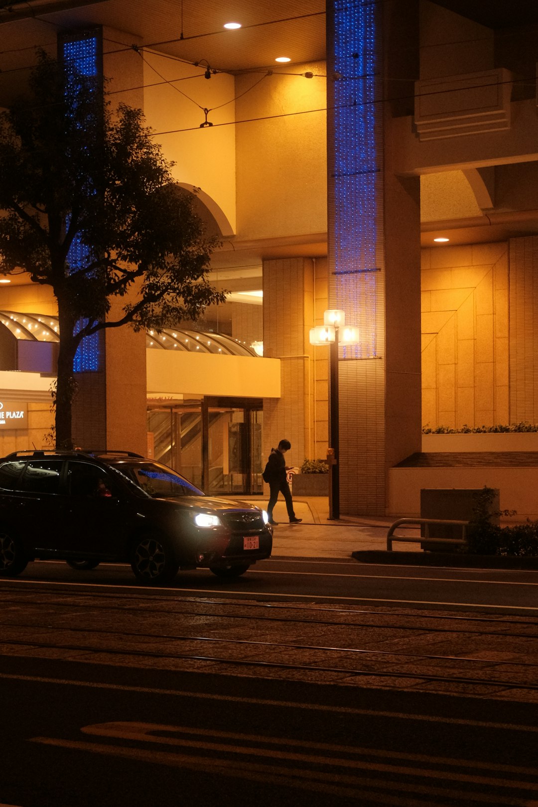 woman in black jacket and black pants standing beside black sedan during night time