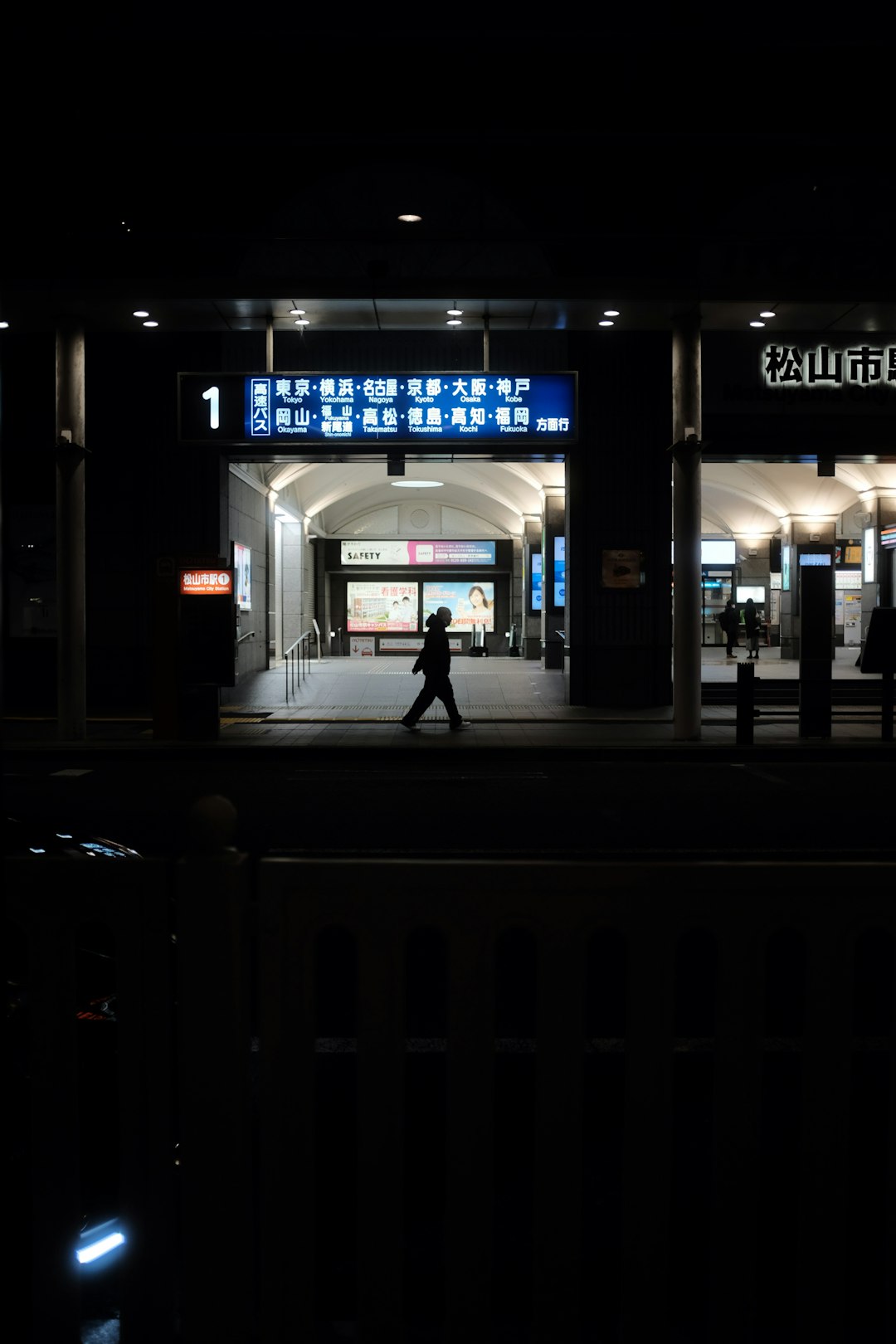 man in black jacket standing near black metal gate during nighttime