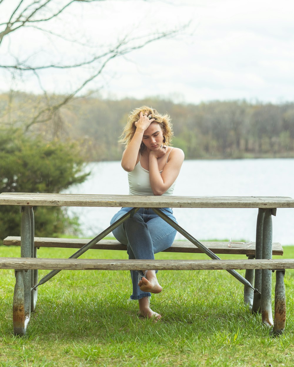 woman in blue denim jeans sitting on brown wooden fence near body of water during daytime