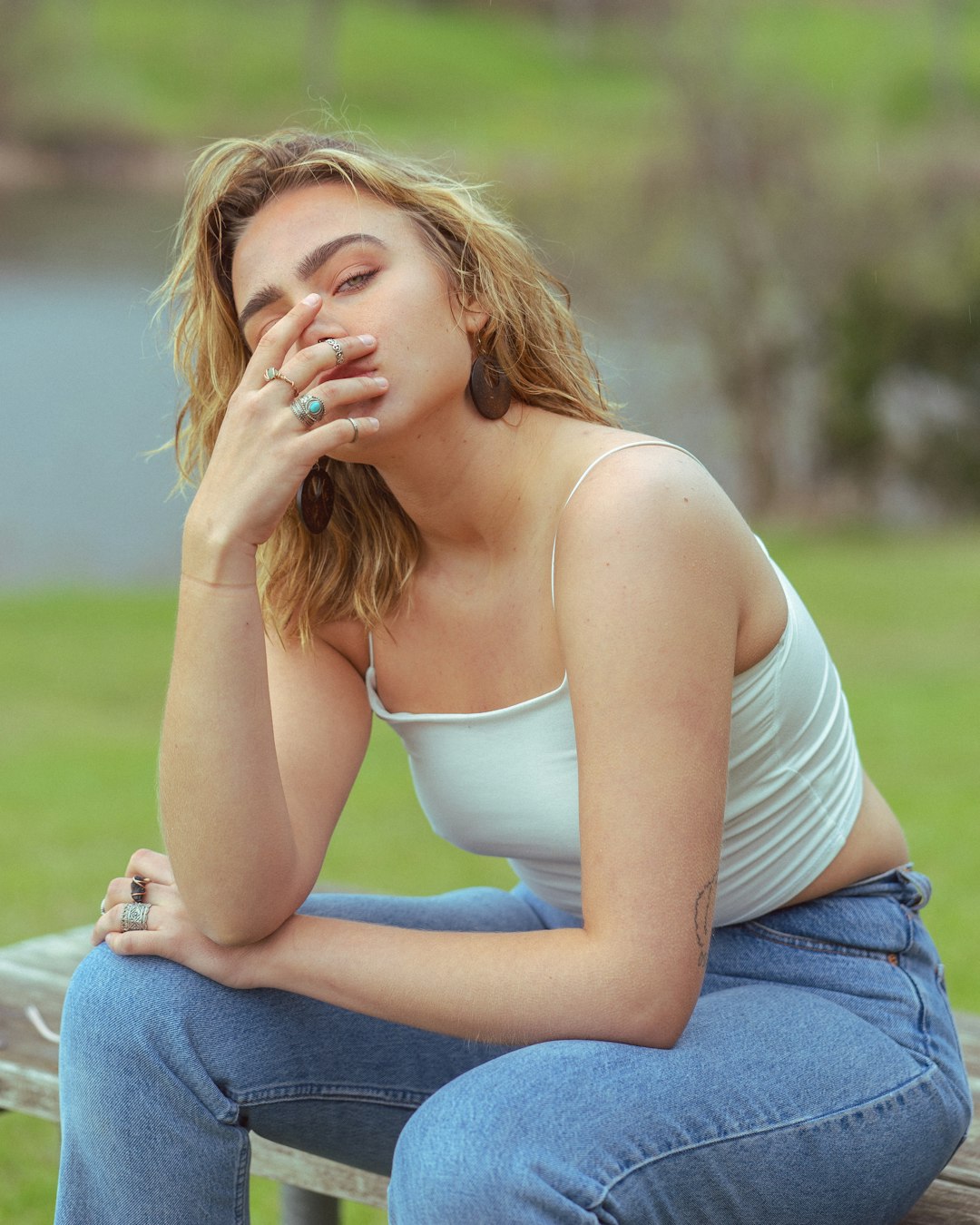 woman in white tank top and blue denim jeans sitting on green grass field during daytime