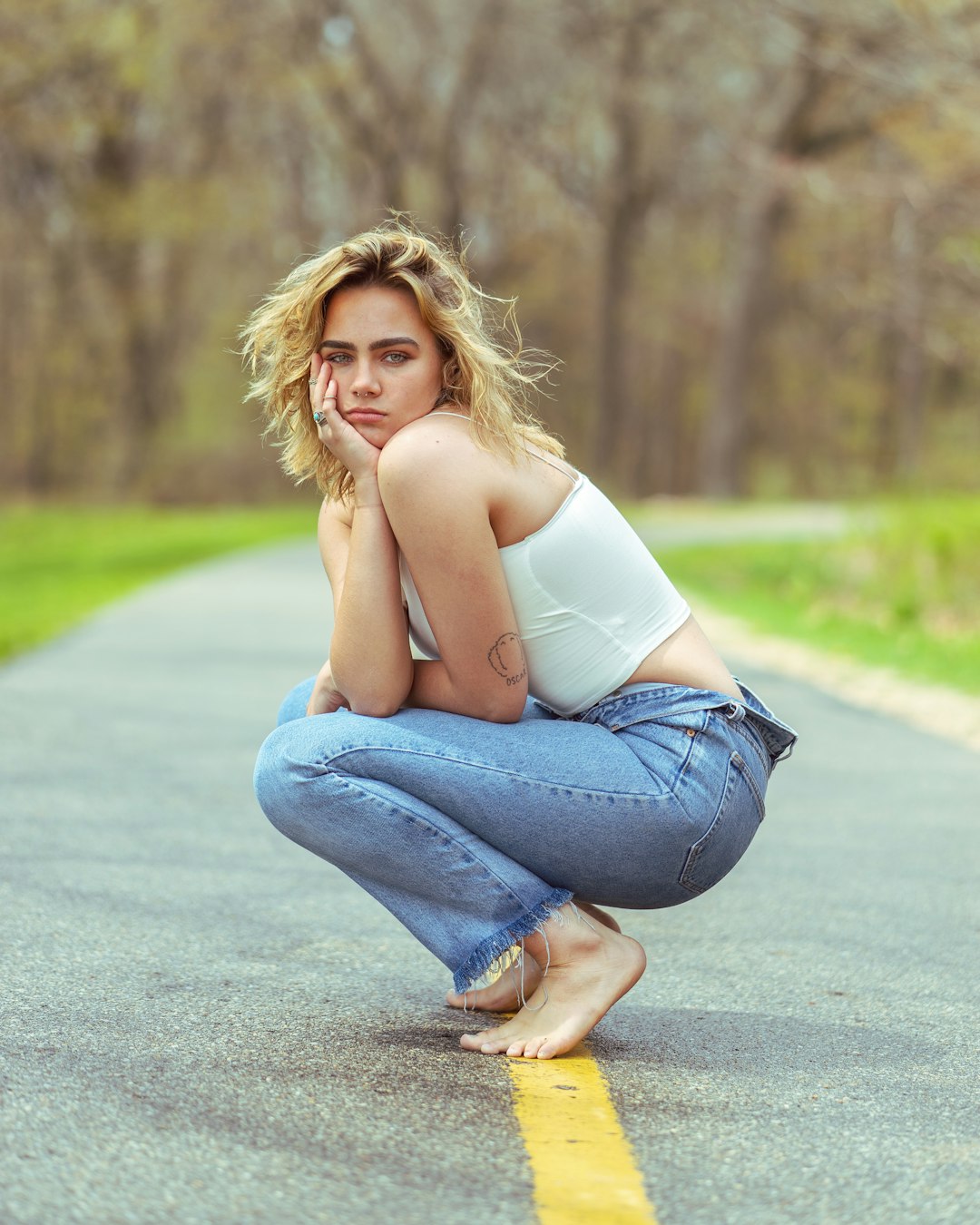 woman in white tank top and blue denim jeans sitting on road during daytime