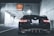 A black BMW car with Texas license plates is parked near the entrance of a tunnel. The tunnel has bright lights along the ceiling, casting a cool illumination. A warning sign above the entrance specifies height restrictions and instructions for when the tunnel is closed.