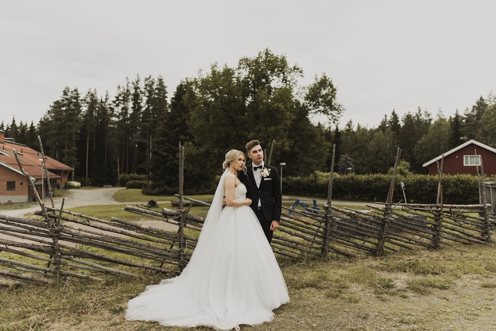 woman in white wedding gown standing on brown wooden fence during daytime