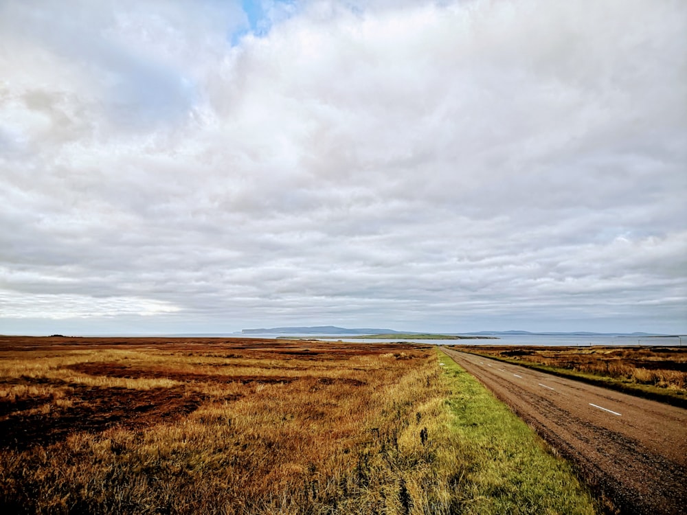 brown grass field under white clouds during daytime