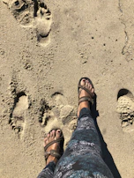 A model walking barefoot on a sandy beach wearing sleek veyra core sandals.