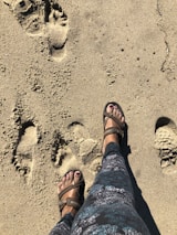 A person wearing sandals walking on a sunny beach.