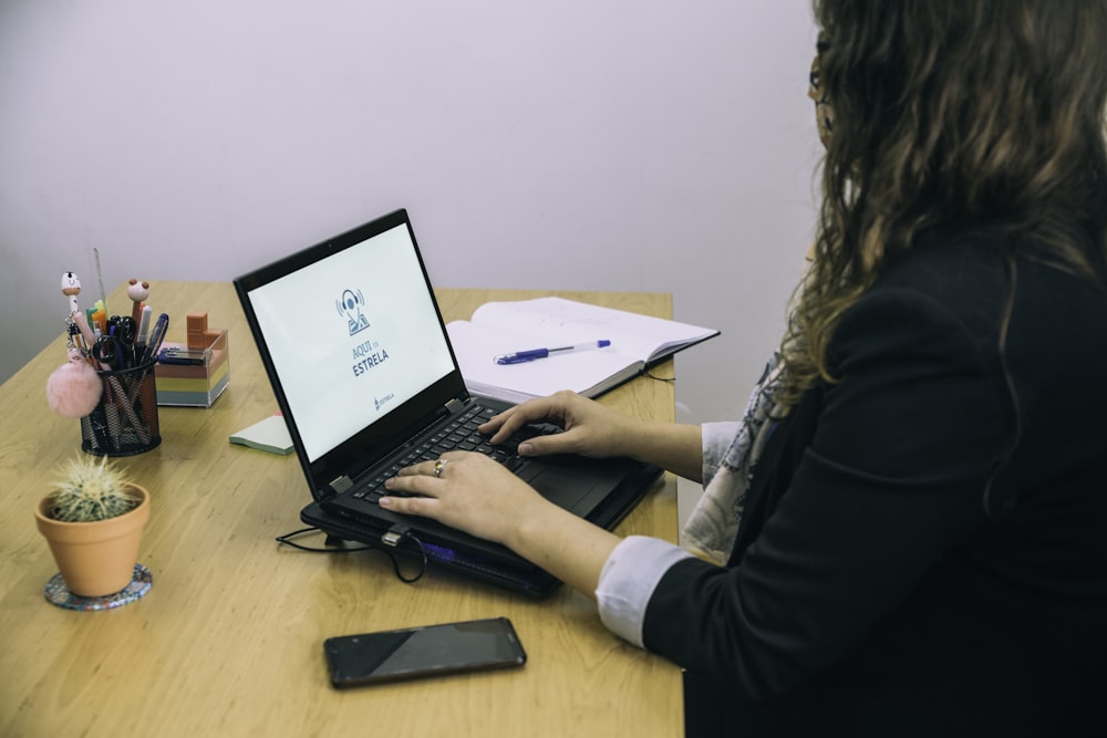 mulher na camisa preta da manga comprida que usa o computador portátil preto