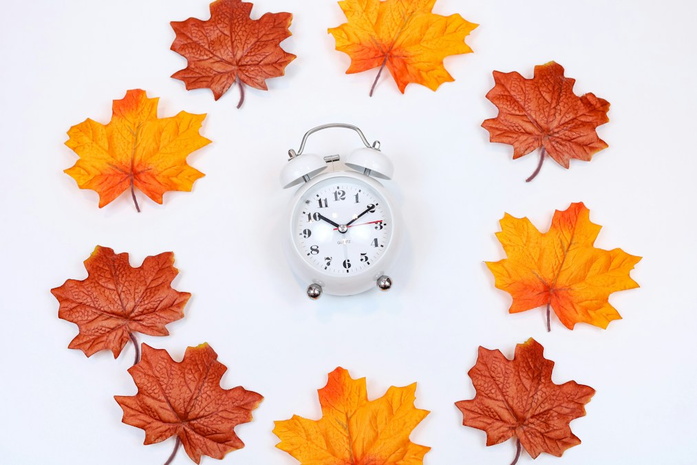 Feuilles d'automne rouges et orangées autour d'une horloge, à l'approche du passage à l'heure d'hiver du 25 octobre 2026