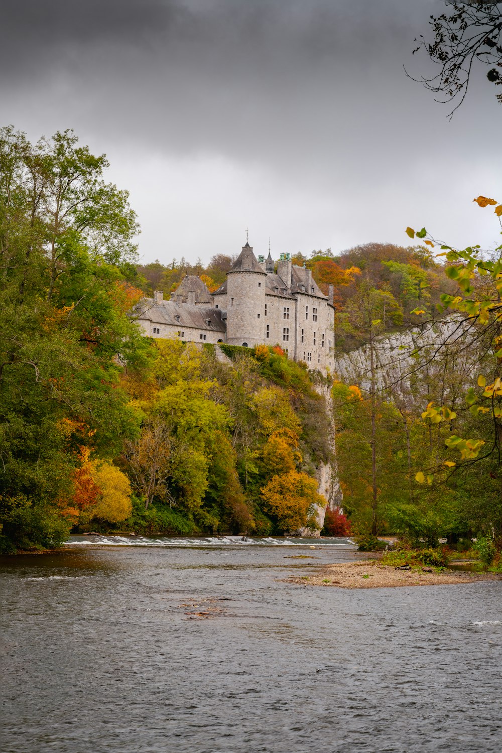 Castillo blanco y gris en árboles verdes al lado del río durante el día