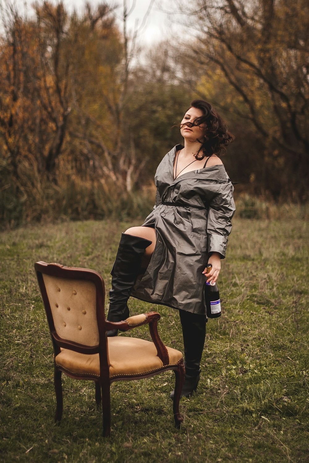 donna in cappotto grigio che si siede sulla poltrona di legno marrone sul campo di erba verde durante il giorno