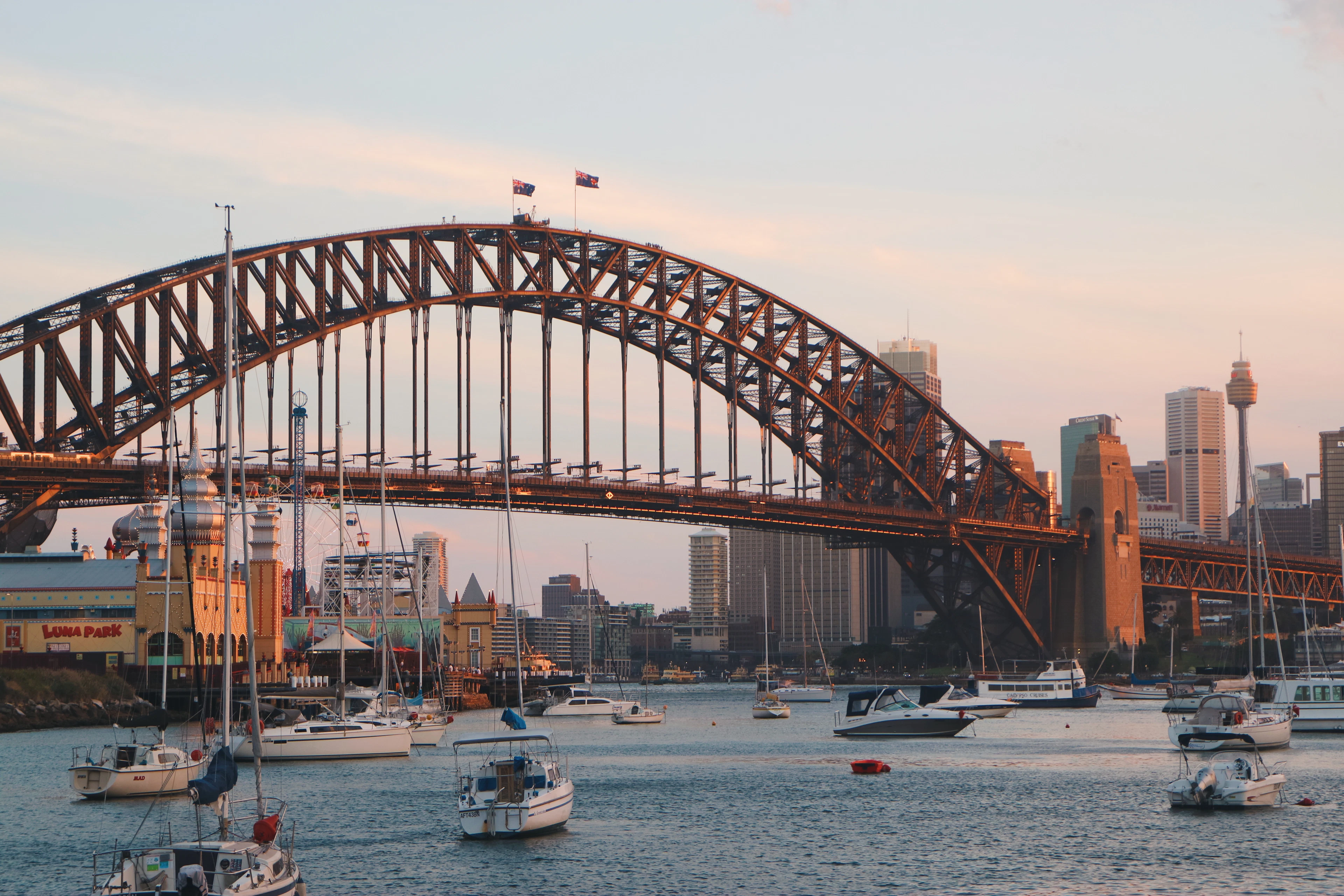 Sydney Harbour Bridge at sunset above Luna Park's entrance and yachts moored in Lavender Bay.