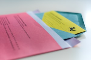 A collection of colorful papers and envelopes, including a pink sheet with text, a yellow paper featuring a black horse silhouette, and a blue envelope, all arranged on a light surface.