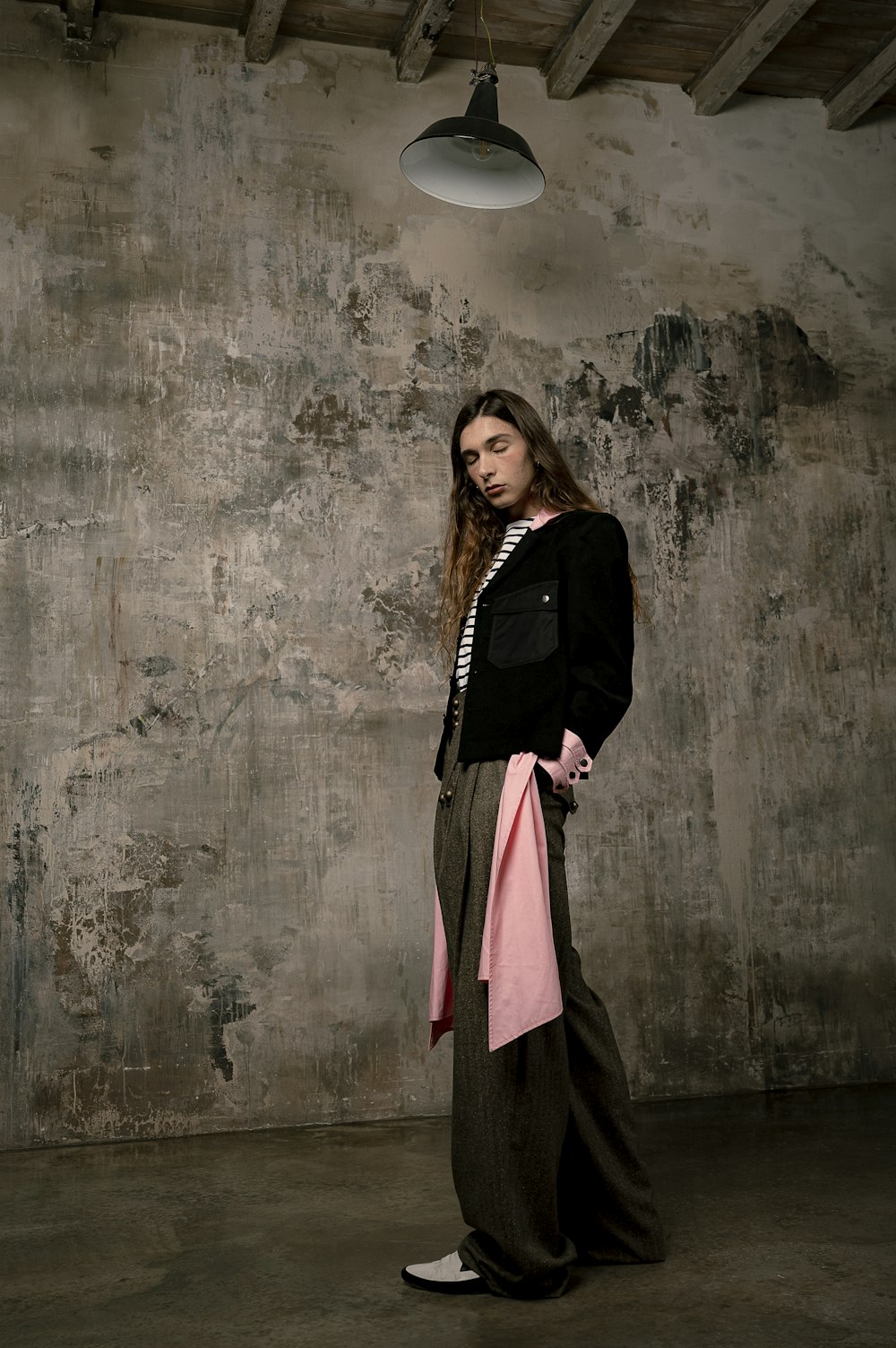 woman in black coat and pink skirt standing beside gray concrete wall